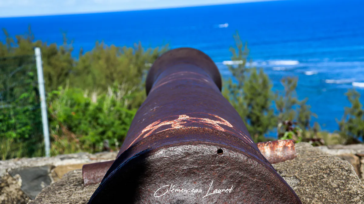 Vue en perspective du fût d'un ancien canon en fonte rouillée pointé vers l'océan bleu à Saint-Leu.