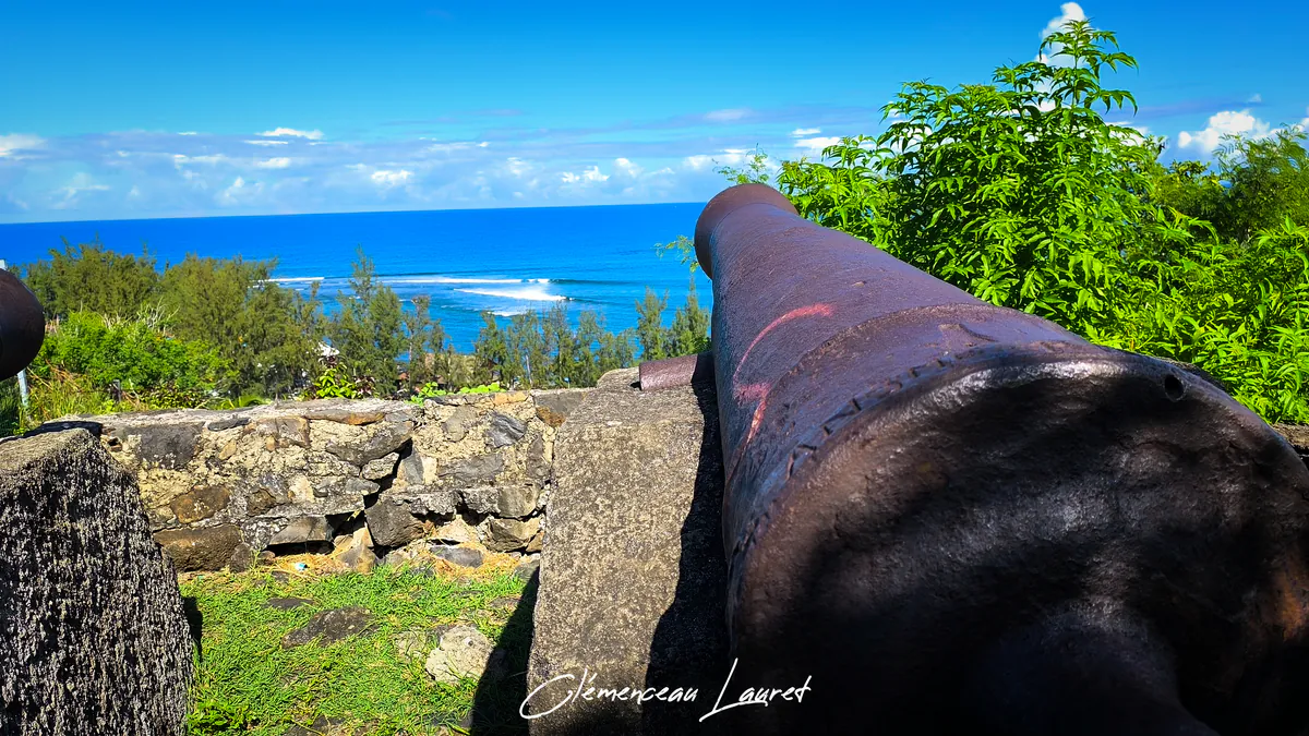 Gros plan sur la culasse massive d'un canon en fonte surplombant les vagues du lagon de Saint-Leu.