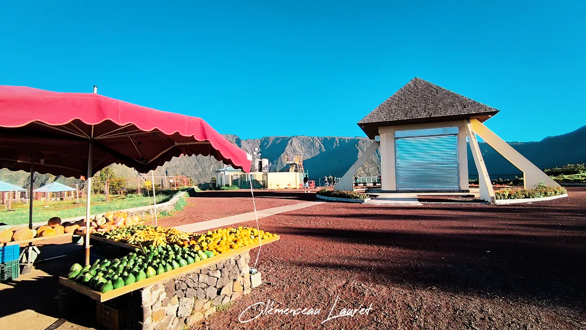 Un marché animé au Belvédère de Bois Court à la Réunion, avec des fruits et légumes frais exposés sous un parasol rouge.