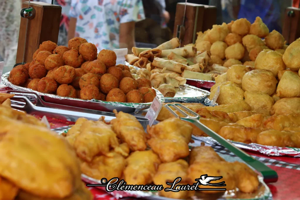Étal de marché chargé d'amuse-bouche réunionnais, samoussas, bouchons et beignets.