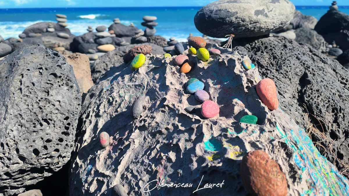 Galets peints en couleurs vives disposés sur les roches sombres de L'Étang-Salé