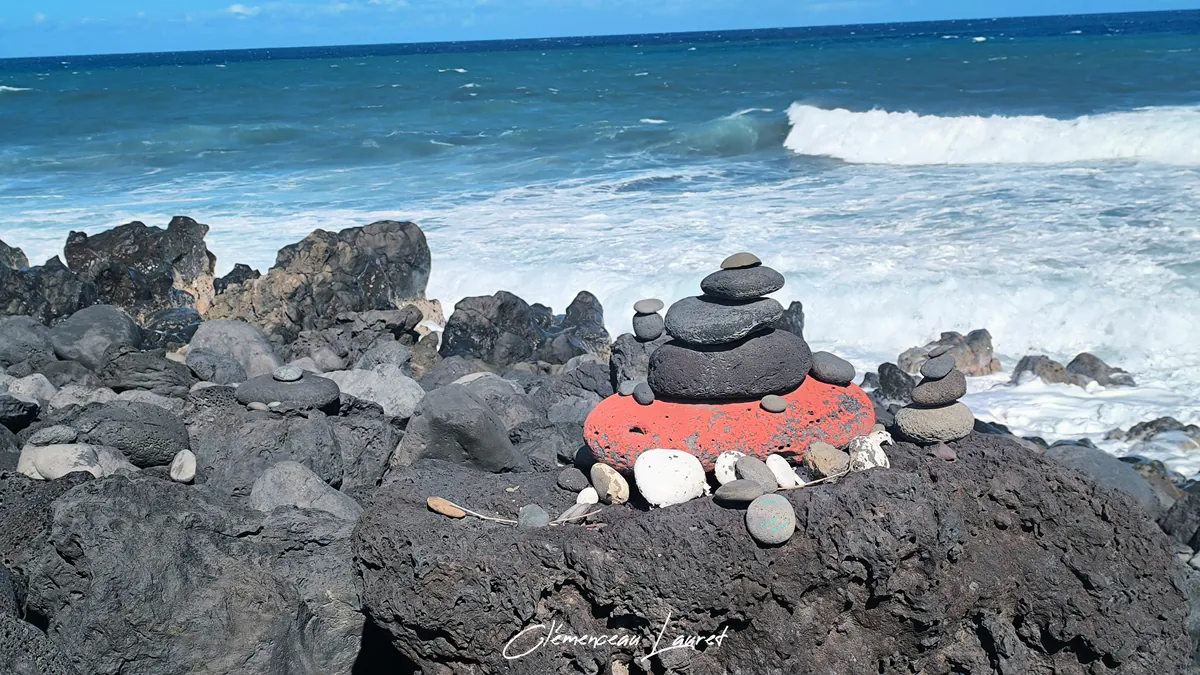 Cairn de pierres avec un galet peint en rouge face à la mer déchaînée à La Réunion
