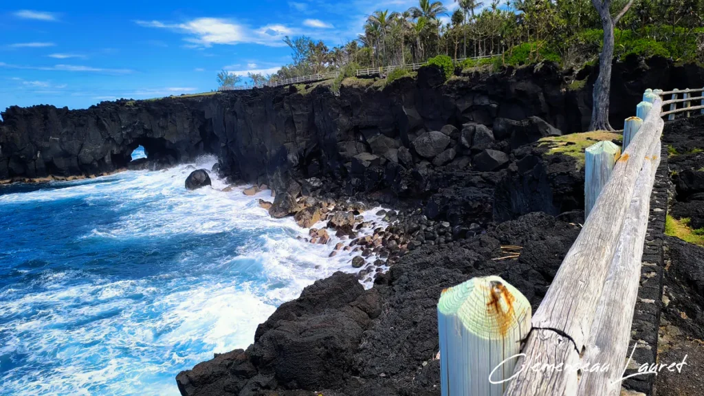 Rambarde en bois le long de la falaise donnant sur l'eau turquoise et l'arche rocheuse du Cap Méchant.