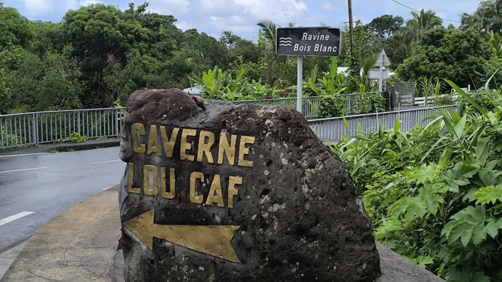 Rocher gravé indiquant Caverne Lou Caf avec une flèche jaune près du panneau Ravine Bois Blanc à Sainte-Rose.