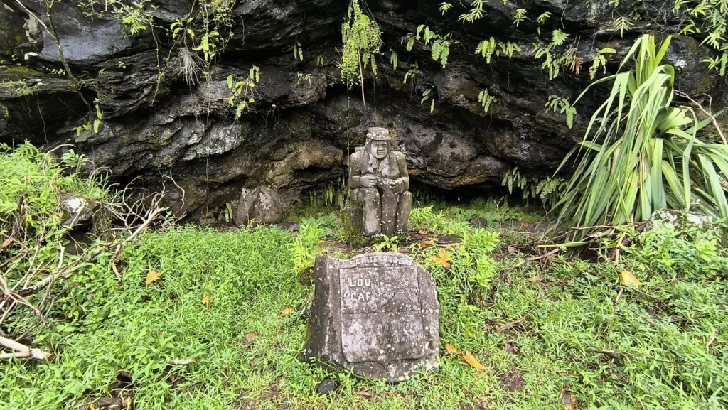 Vue rapprochée de la statue de Lou Caf assis avec le blason en pierre gravé au premier plan à Sainte-Rose.