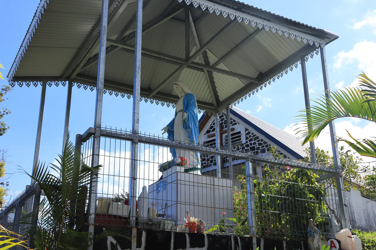 Statue de la Vierge Marie voilée de bleu sous un abri métallique à structure ajourée.