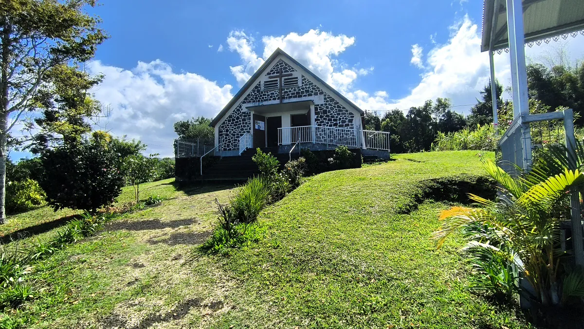 Chapelle en pierres sombres au sommet d'un terrain en herbe sous un ciel bleu nuageux.