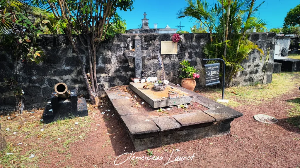 Vue rapprochée de la tombe du pirate La Buse avec sa croix en pierre, son canon et ses objets commémoratifs.