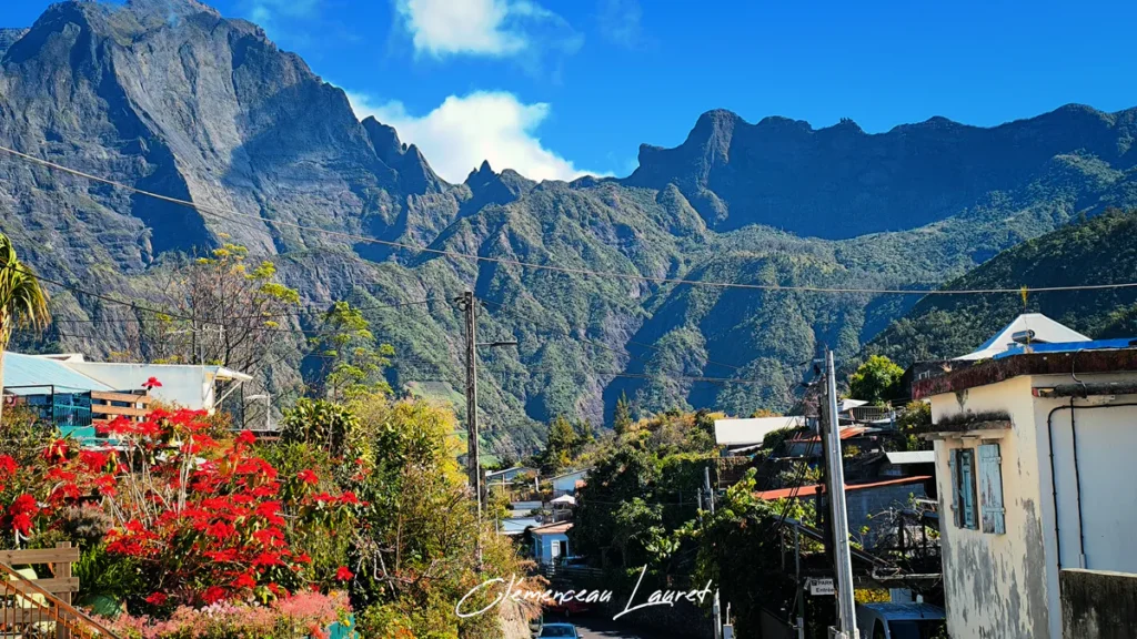 Vue d'une ruelle bordée de poinsettias rouges éclatants s'ouvrant sur le rempart massif de montagnes vertes du cirque de Cilaos.