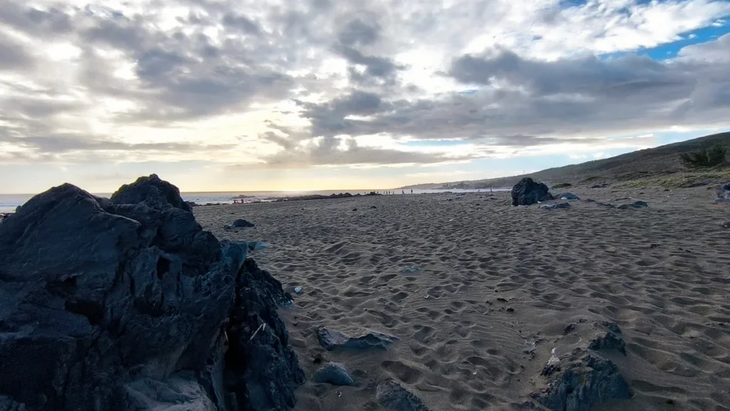 Perspective sur le rivage volcanique de l'Étang-Salé avec de grandes formations rocheuses noires au premier plan et des silhouettes à l'horizon.