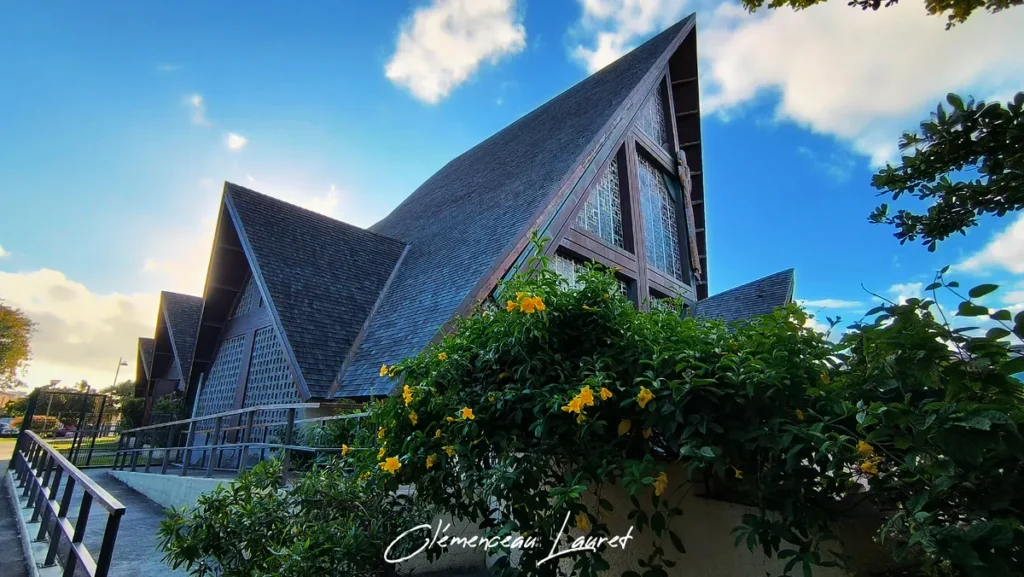 Face latérale gauche de l'église du Bon Pasteur à Saint-Pierre avec un buisson de fleurs jaunes au premier plan.