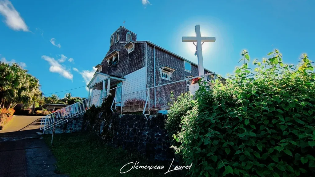 Photographie en contre-plongée de la croix blanche dressée devant l'église des Lianes à Saint-Joseph sous le soleil de La Réunion.