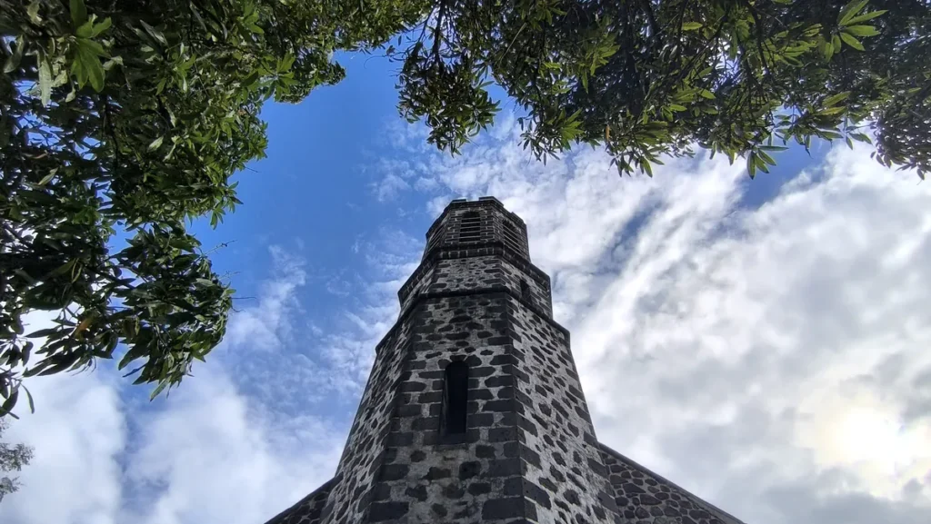Vue en contre-plongée du clocher en pierre de l'église encadrée par le feuillage vert des arbres.