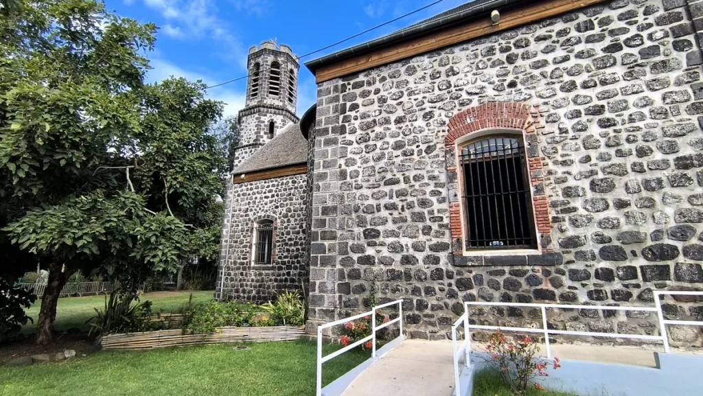 Façade latérale en pierres de taille avec fenêtres à barreaux et ruelle d'accès aménagée.