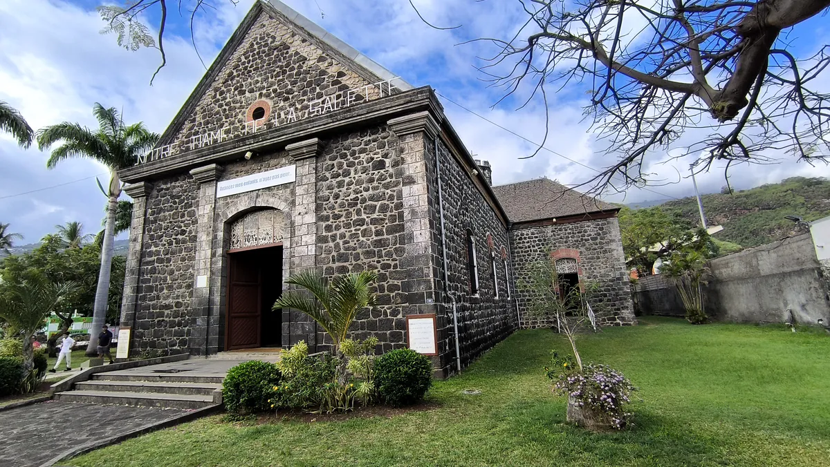 Façade principale en basalte de l'église Notre-Dame-de-la-Salette avec son entrée ouverte et son fronton gravé.