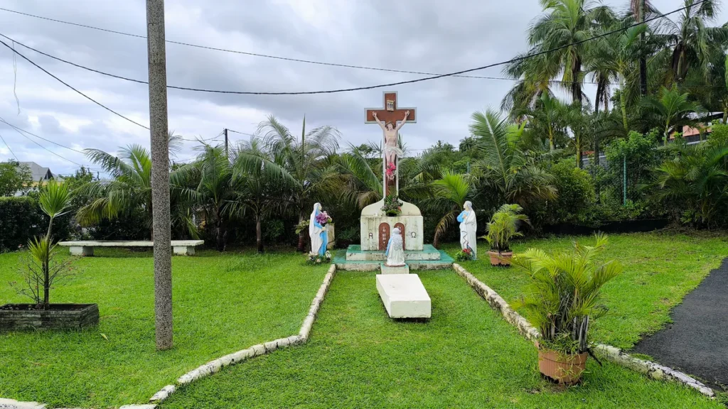 Calvaire en bois sculpté représentant le Christ en croix avec statues de la Vierge sur une pelouse verte