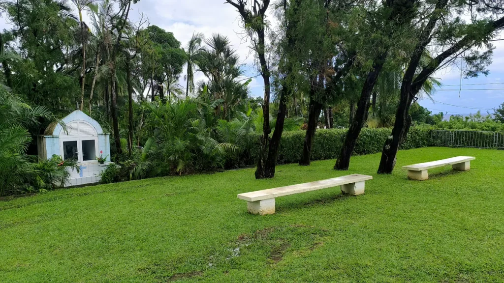 Petit oratoire bleu et blanc au fond d'un jardin bordé de bancs sous une végétation tropicale