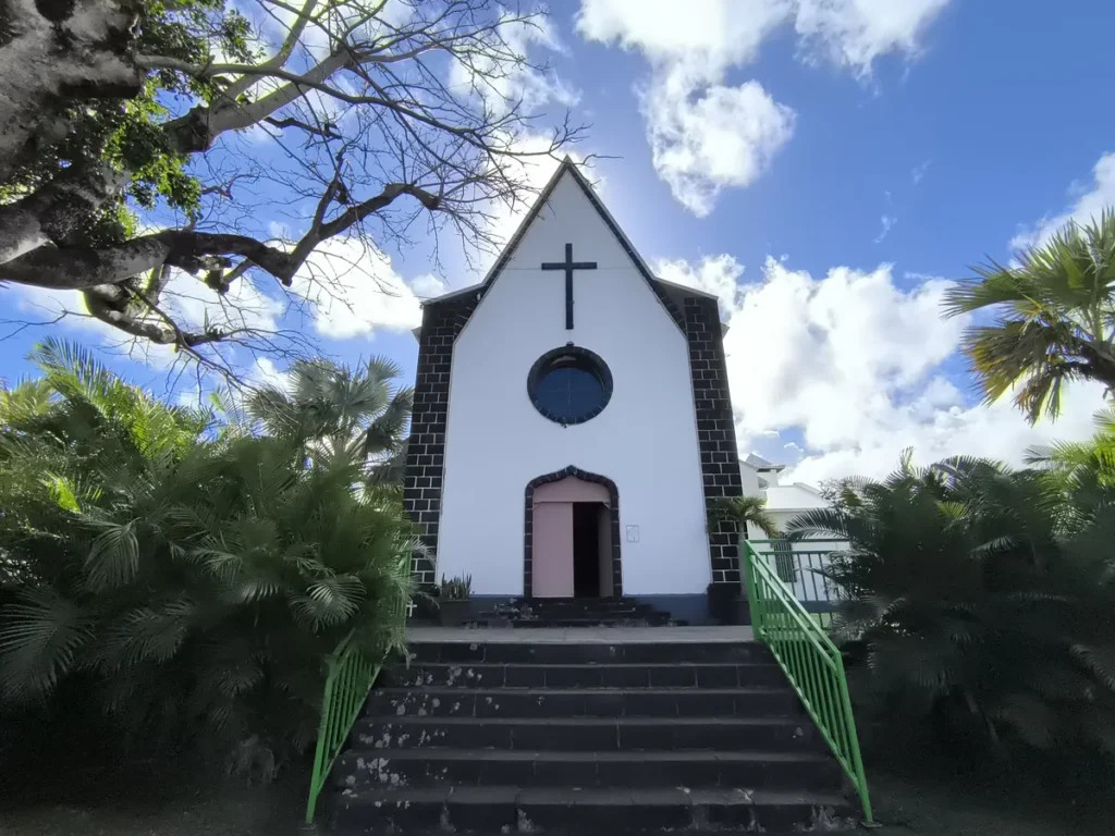 Vue frontale de l'église Saint-Athanase de Vincendo entourée de végétation tropicale