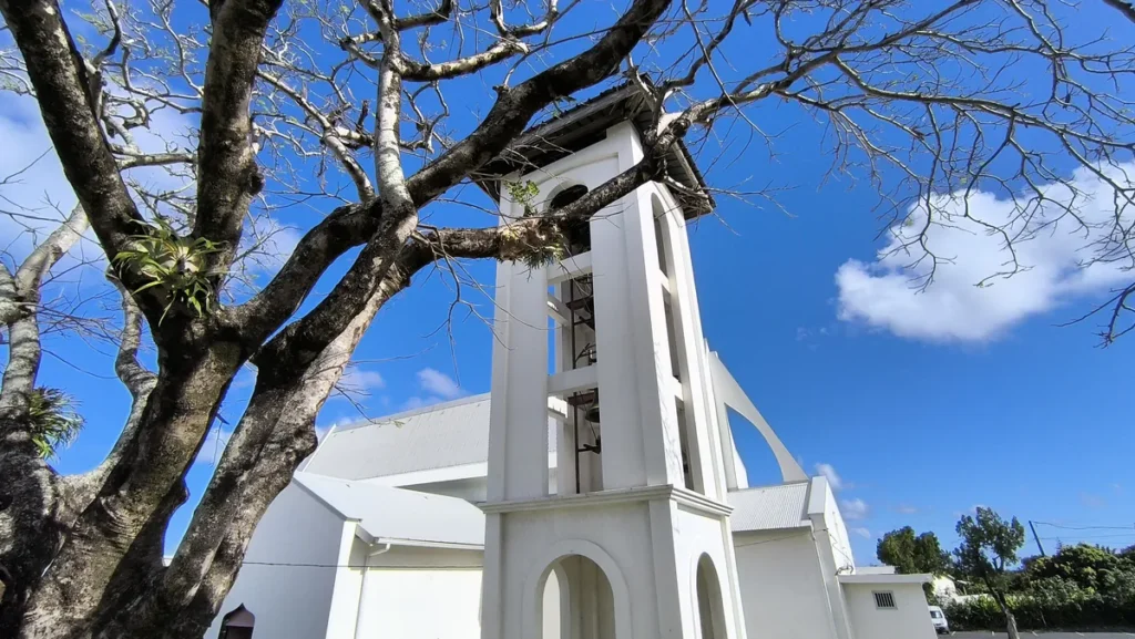 Clocher séparé et bâtiment de l'église Saint-Athanase de Vincendo encadrés par un arbre