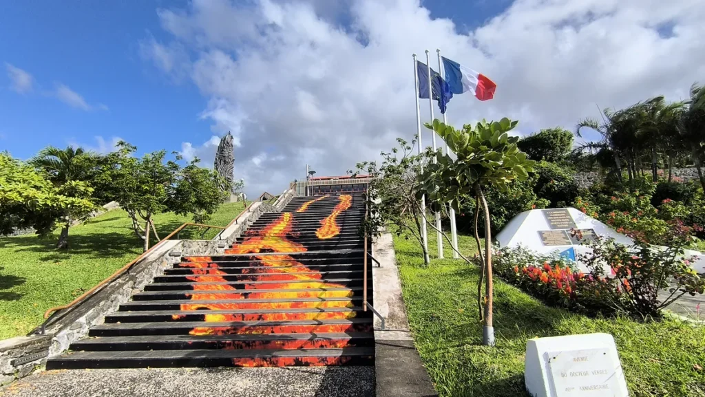 Escalier peint en motif de lave au milieu d'un parc avec drapeaux et palmiers à Sainte-Rose