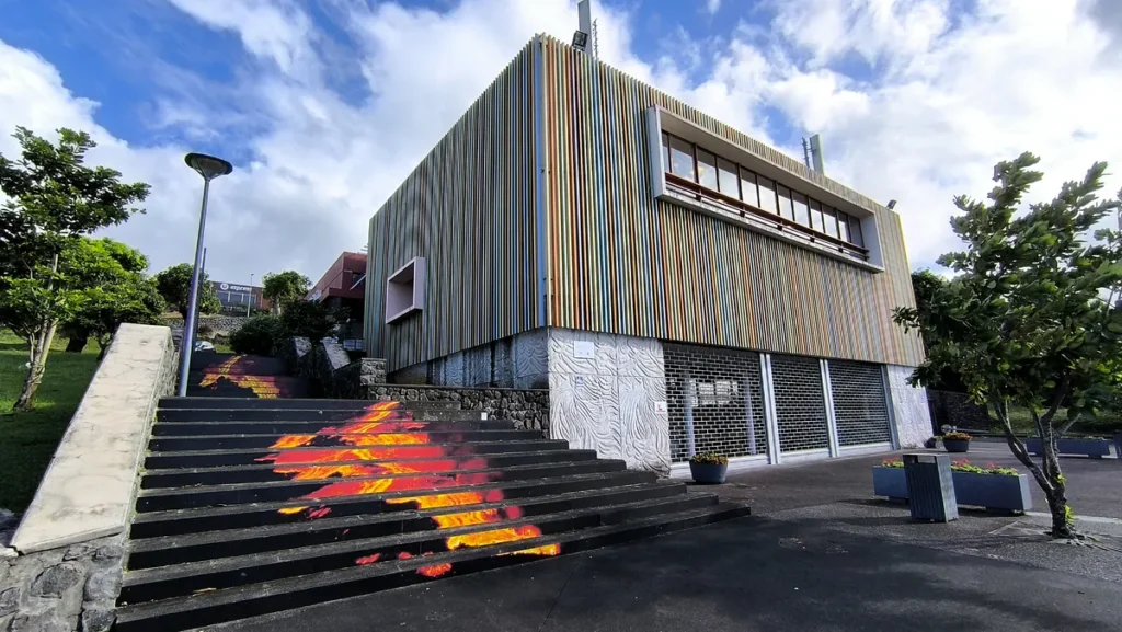 Angle du bâtiment au revêtement en lattes de bois colorées et escalier décoré d'une fresque de lave