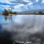 Grandes ondulations à la surface de l'eau sombre de l'Étang du Gol avec la côte et les montagnes au loin.