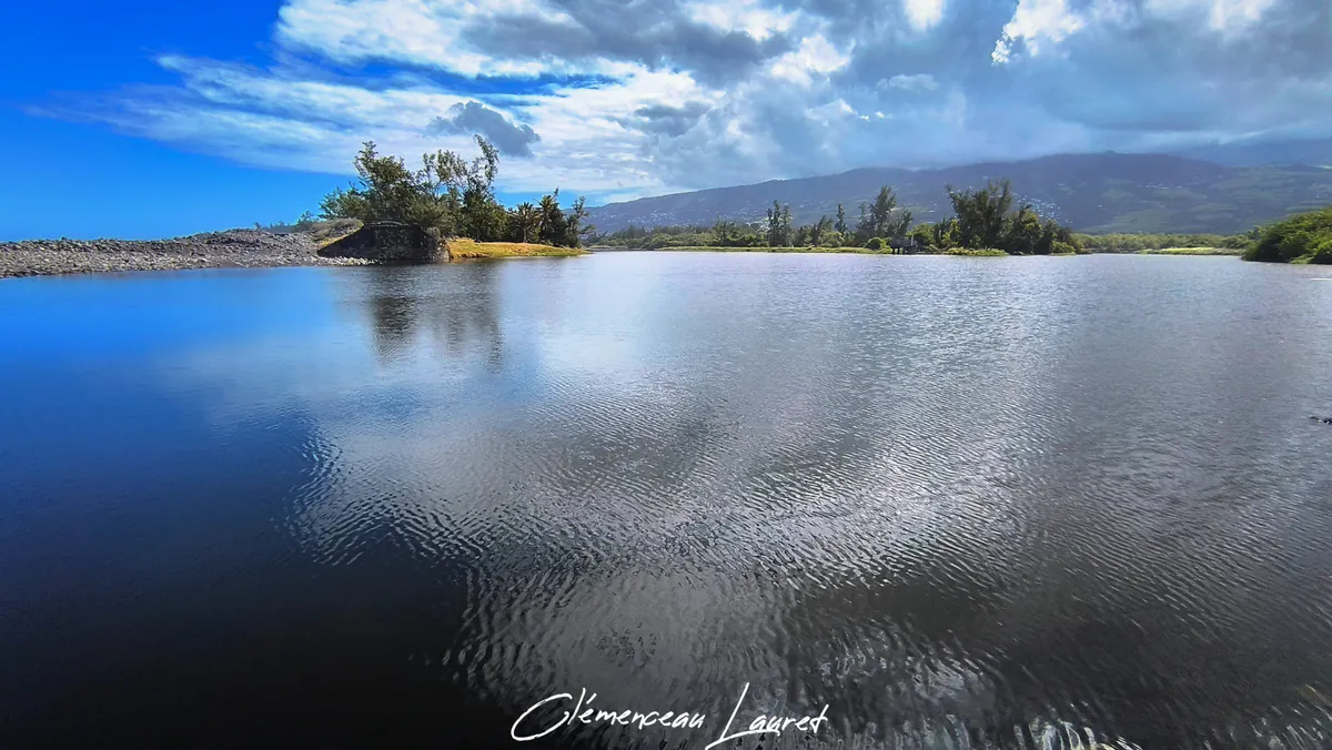 Grandes ondulations à la surface de l'eau sombre de l'Étang du Gol avec la côte et les montagnes au loin.
