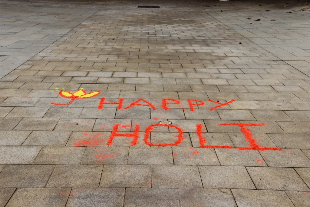 Inscription Happy Holi tracée au sol avec de la poudre rouge et un dessin de fleur jaune sur le pavé.