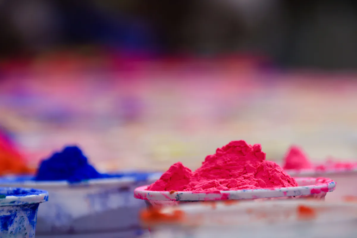 Coupelles remplies de poudres de pigments rose fluo et bleu vif posées en rangée pour la fête de Holi.