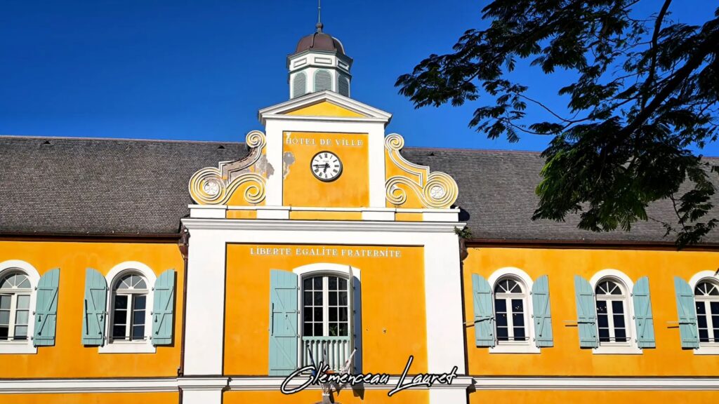 Fronton jaune de l'hôtel de ville de Saint-Pierre avec horloge et devise républicaine.