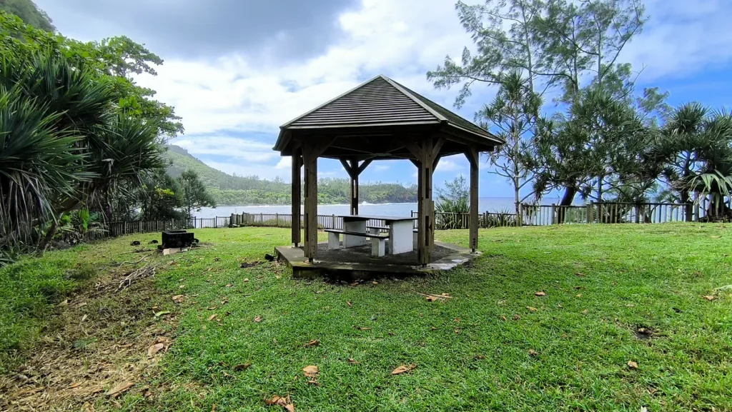 Kiosque couvert avec table sur gazon ombragé par des arbres en bord de mer à La Source Sainte-Rose.