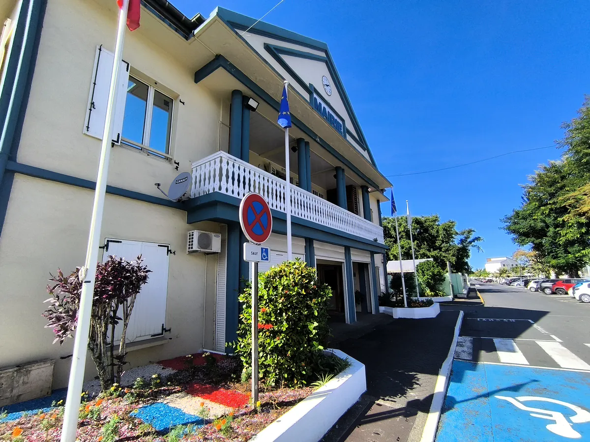 Façade de la mairie de Sainte-Suzanne à La Réunion avec ses colonnes bleues, son balcon blanc à balustres et un parterre aux couleurs du drapeau français.