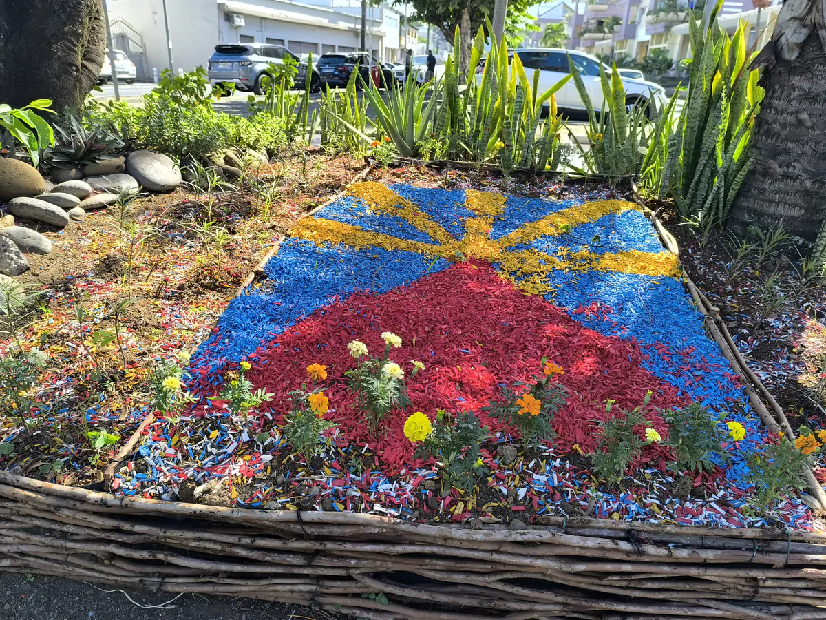 Mosaïque végétale et copeaux de bois reproduisant le drapeau réunionnais Lö Mahavéli dans un parterre tressé en bois.