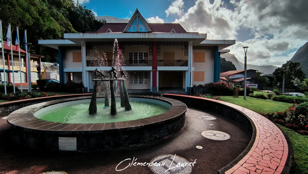 Fontaine en pierre avec jet d'eau devant le bâtiment de la mairie de Salazie sous un ciel nuageux à La Réunion