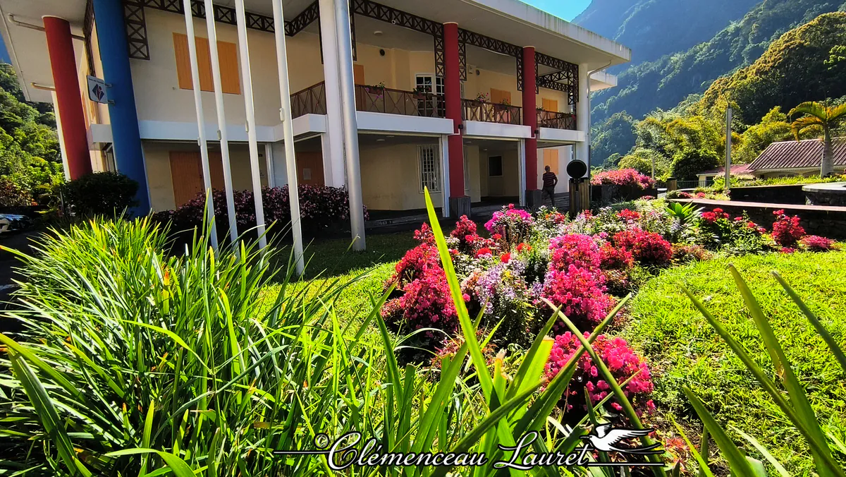 Parterre de fleurs roses et rouges au premier plan avec la mairie de Salazie et les montagnes en fond