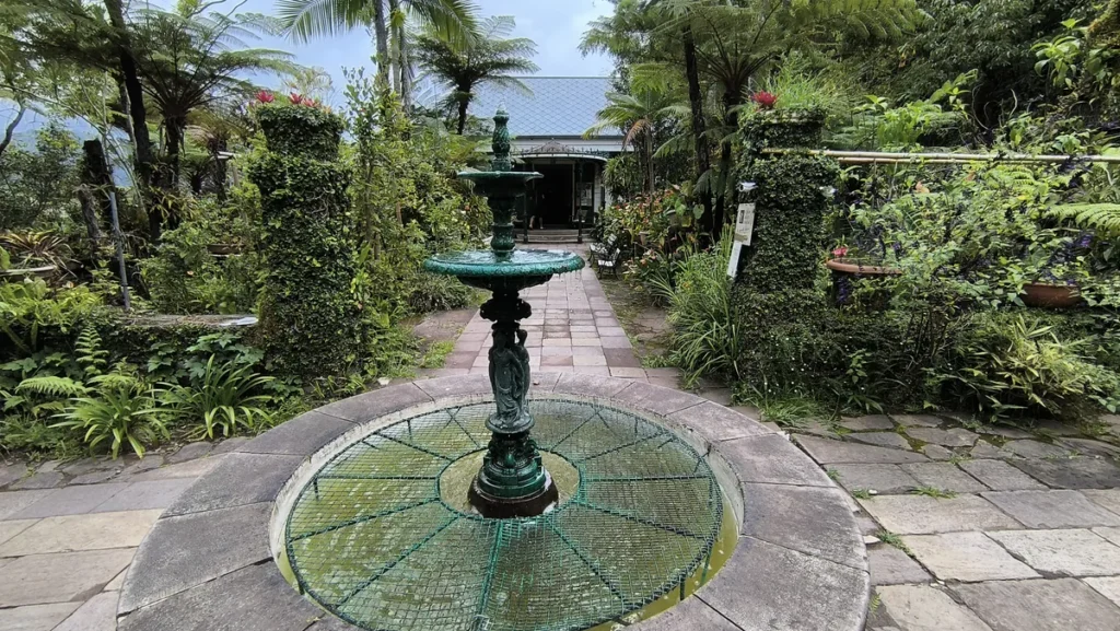 Fontaine en fonte verte au centre d'un bassin en pierre bordé d'allées dallées dans le jardin.