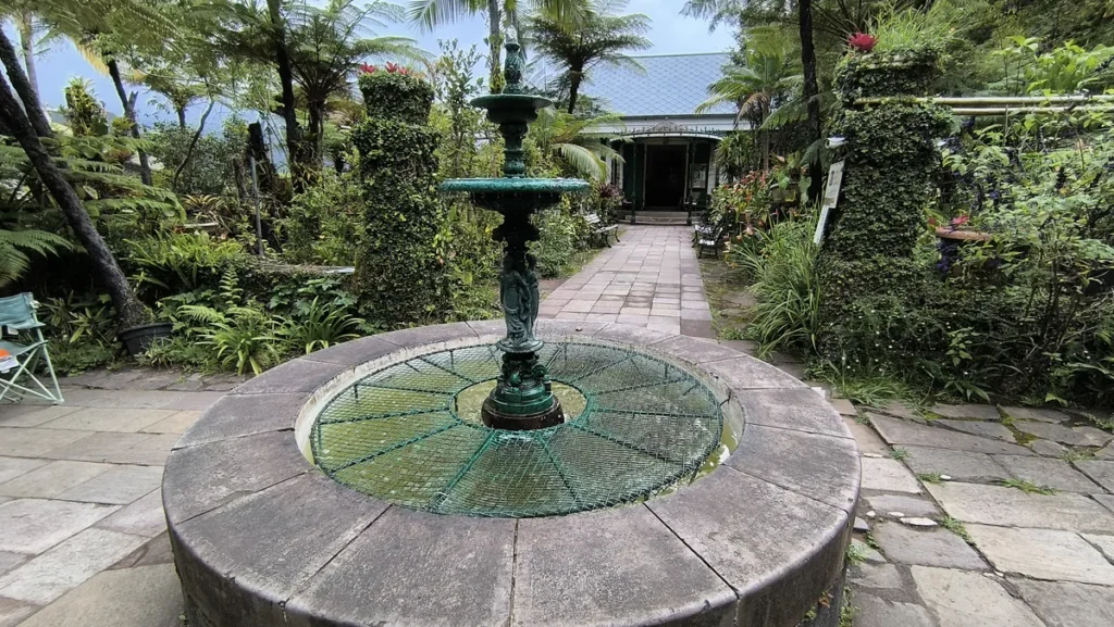 Fontaine en fonte verte au centre d'un jardin tropical devant la Maison Folio à Hell-Bourg