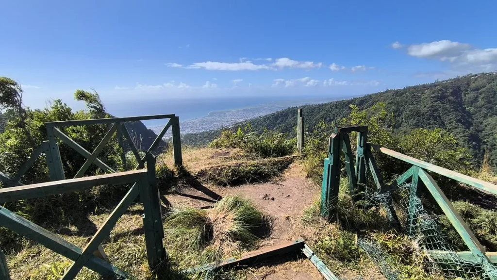 Passerelle et belvédère en bois ouvrant sur un précipice et une vue dégagée sur l'océan.