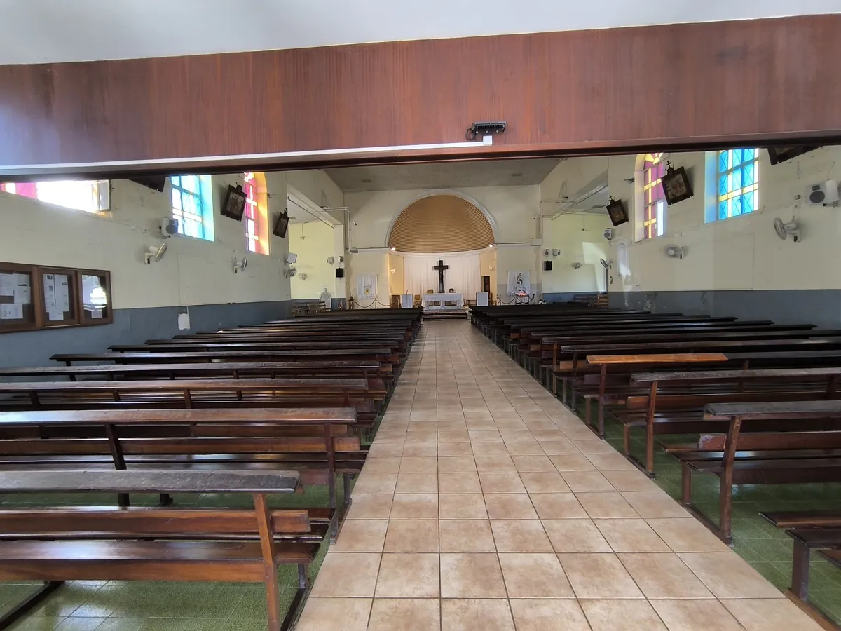 Vue en perspective de l'allée centrale et des bancs en bois à l'intérieur de l'église Saint-François-Xavier avec vitraux colorés et autel au fond.