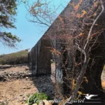 Contre-plongée sur la structure en maçonnerie de pierre sombre du pont de la ravine Colimaçon longeant une route.