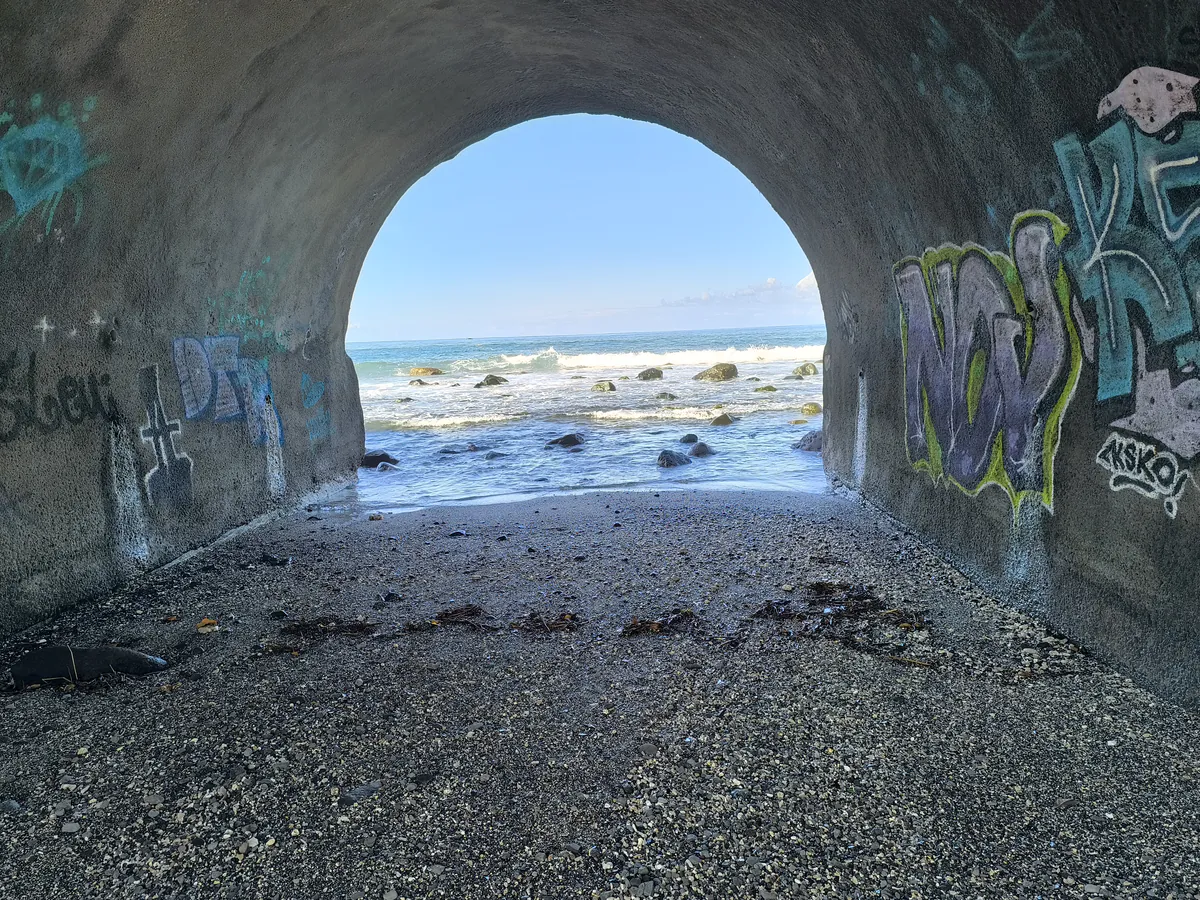 Vue de l'océan Indien à travers un tunnel voûté en béton couvert de graffitis à la Ravine des Colimaçons, Saint-Leu.