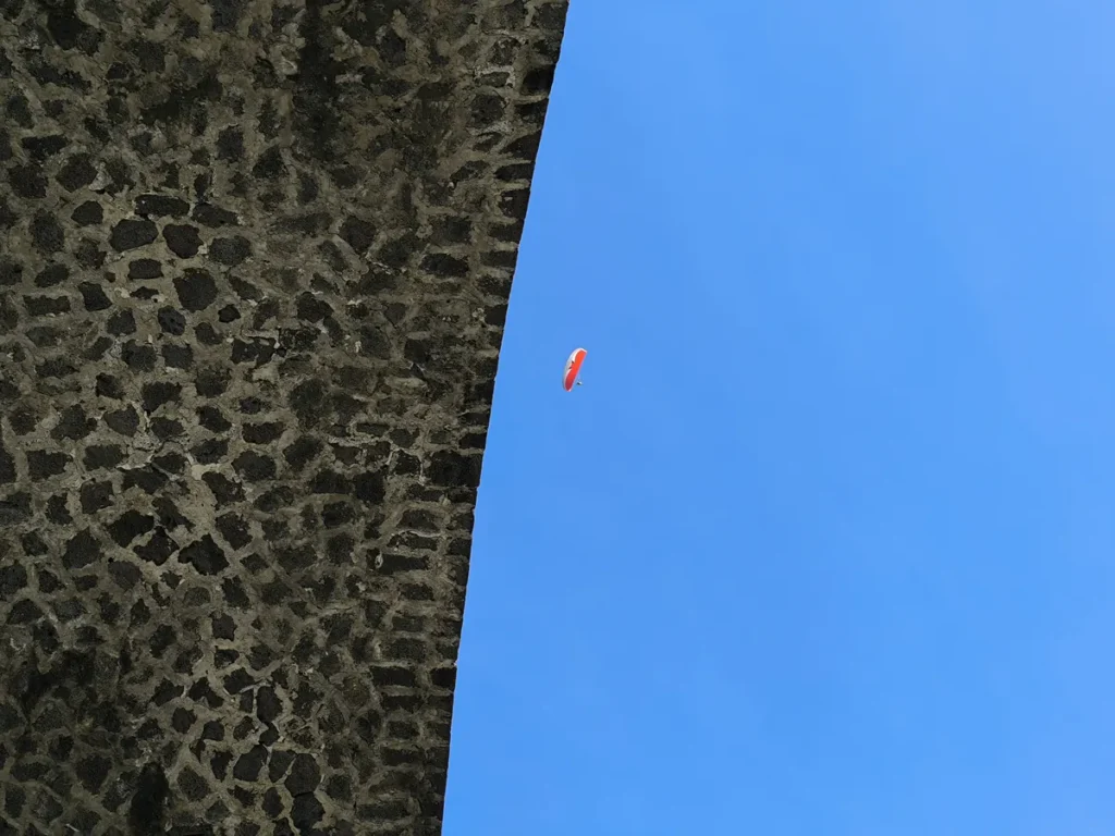 Gros plan du bord en maçonnerie du viaduc de la Ravine des Colimaçons à Saint-Leu et un parapente rouge et blanc dans le ciel.