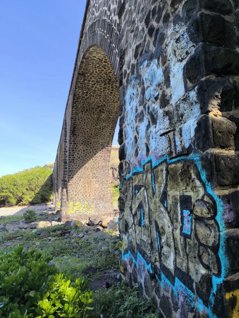 Vue en contre-plongée d'une pile de viaduc en pierre gravée de tags colorés à la Ravine des Colimaçons, Saint-Leu.