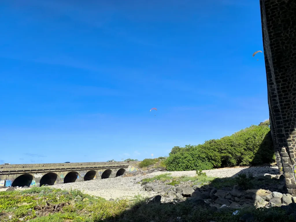 Vue d'ensemble de la Ravine des Colimaçons à Saint-Leu montrant le pont routier à arches, le viaduc et deux parapentes dans le ciel.