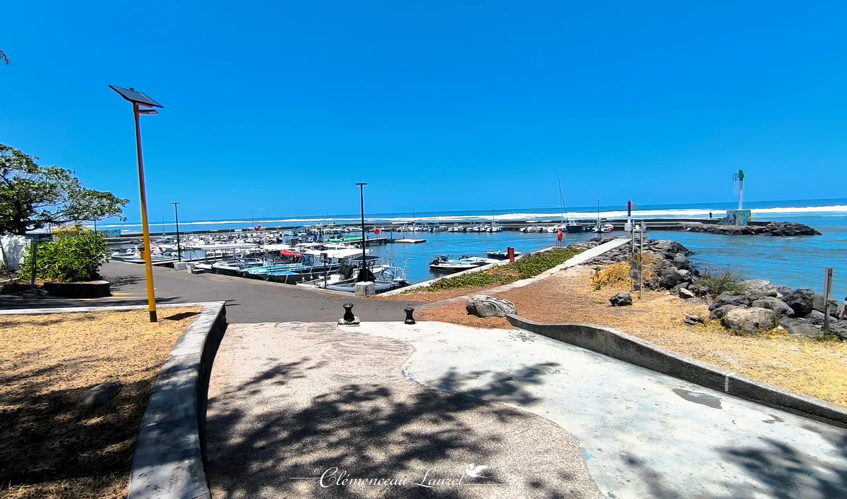 Rampes d'accès en béton menant au port de Saint-Leu avec des bateaux amarrés sous un ciel bleu intense.
