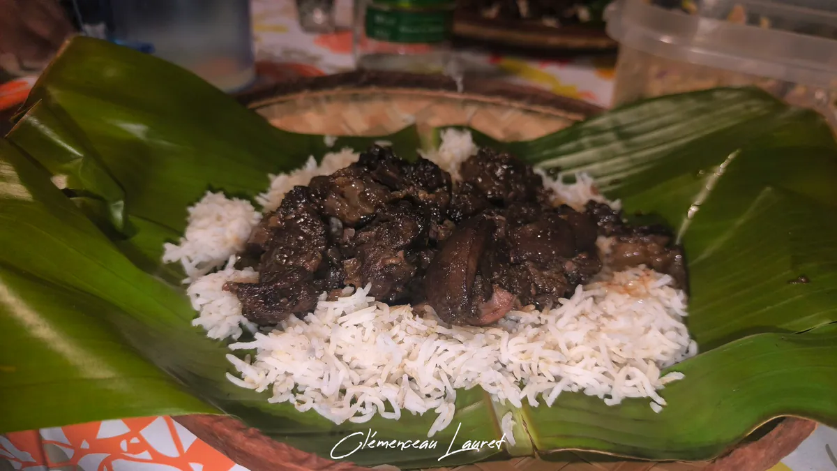 Plan rapproché sur les morceaux de tangue en sauce brune disposés sur le riz blanc chaud et la feuille de bananier.