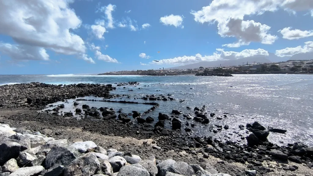 Bassin d'eau délimité par des pierres volcaniques sur un rivage rocheux à marée basse.