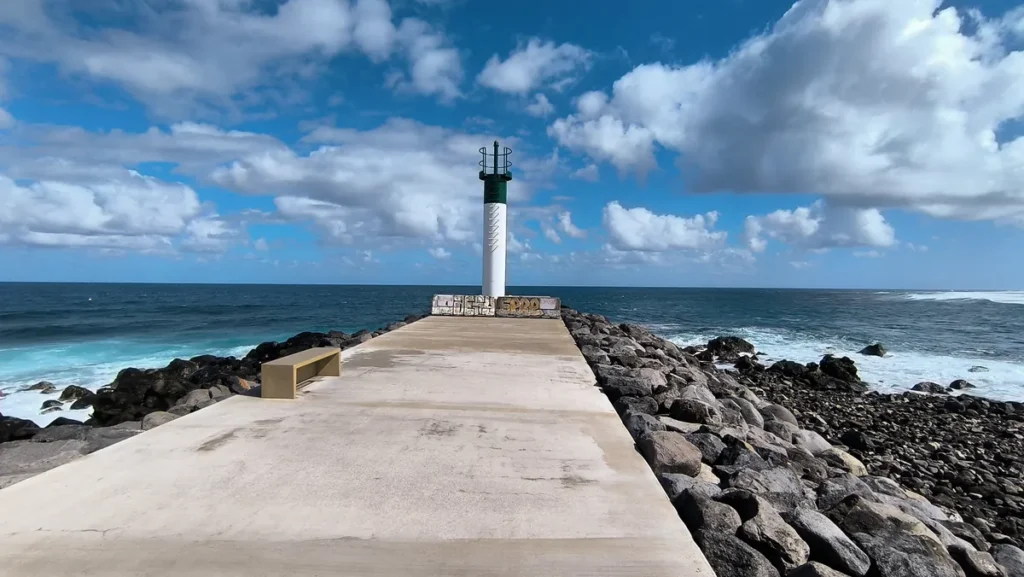 Tourelle de signalisation maritime verte et blanche au bout d'une jetée en béton au bord de l'eau.