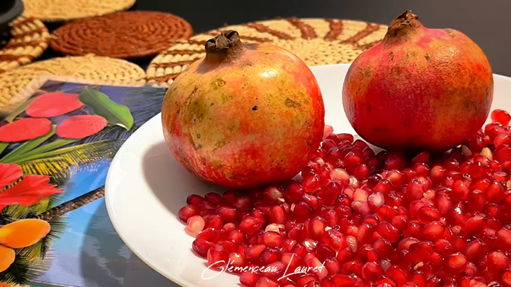 Deux grenades entières posées sur une assiette blanche remplie d'arilles rouge rubis étincelants.