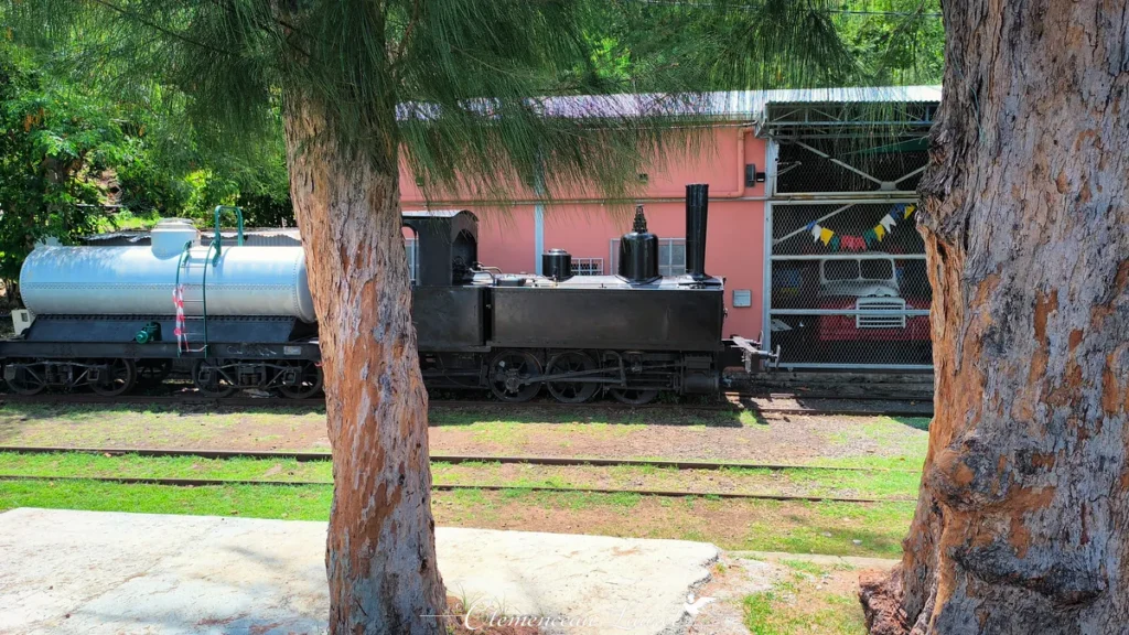 Locomotive à vapeur noire et wagon-citerne stationnés sur les rails à La Grande Chaloupe sous une lumière ensoleillée.